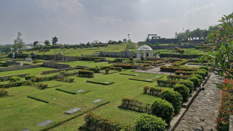 Taman pemakaman San Diego Hills yang tertata dengan pagar tanaman, jalur batu, dan pergola putih